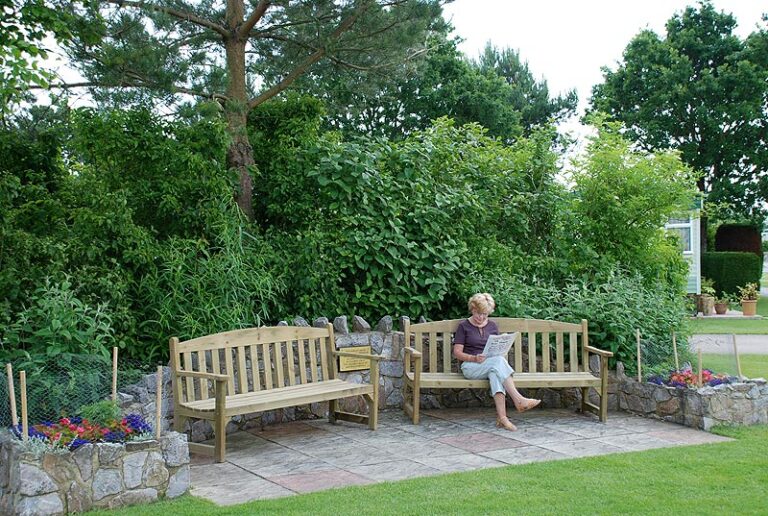 Wooden benches in a sheltered garden with a person sitting and the sea visible through the trees