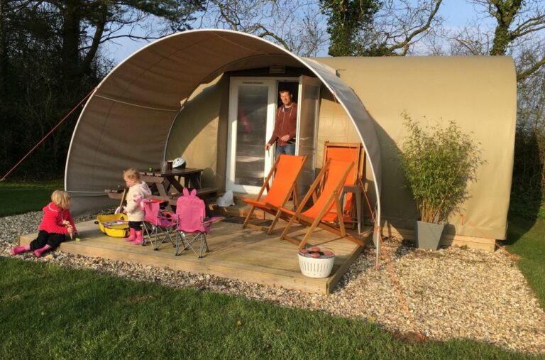 A family sitting in orange chairs outside a glamping pod on the grass at Oakdown