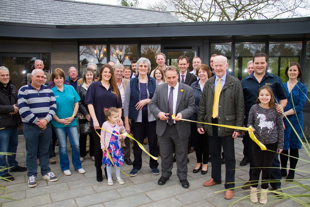 A group gathered outside the new reception building for the ribbon cutting, with a gold ribbon across the doorway