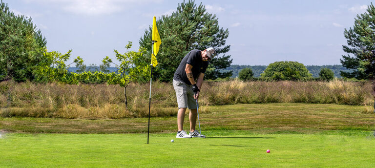A golfer putting on a green with the flag in the hole and open Devon countryside beyond