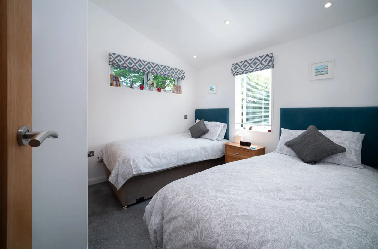Stylish lodge bathroom with full-size bath and overhead shower, modern white fixtures, grey tile accents, and natural light from a high-set window.