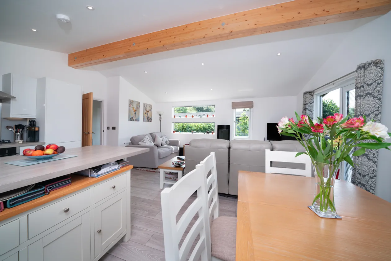 Comfortable and stylish lodge lounge with neutral tones, exposed timber beam, and views through to the well-appointed kitchen and dining area.