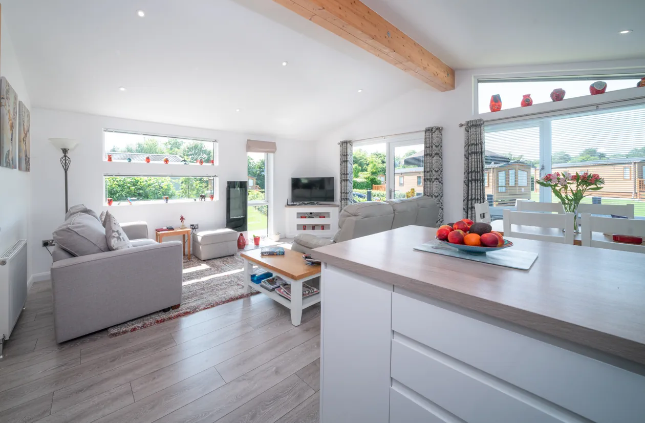 Bright and airy dining space with fresh flowers and a breakfast bar, seamlessly connecting to a modern kitchen and cosy lounge in a spacious holiday lodge.