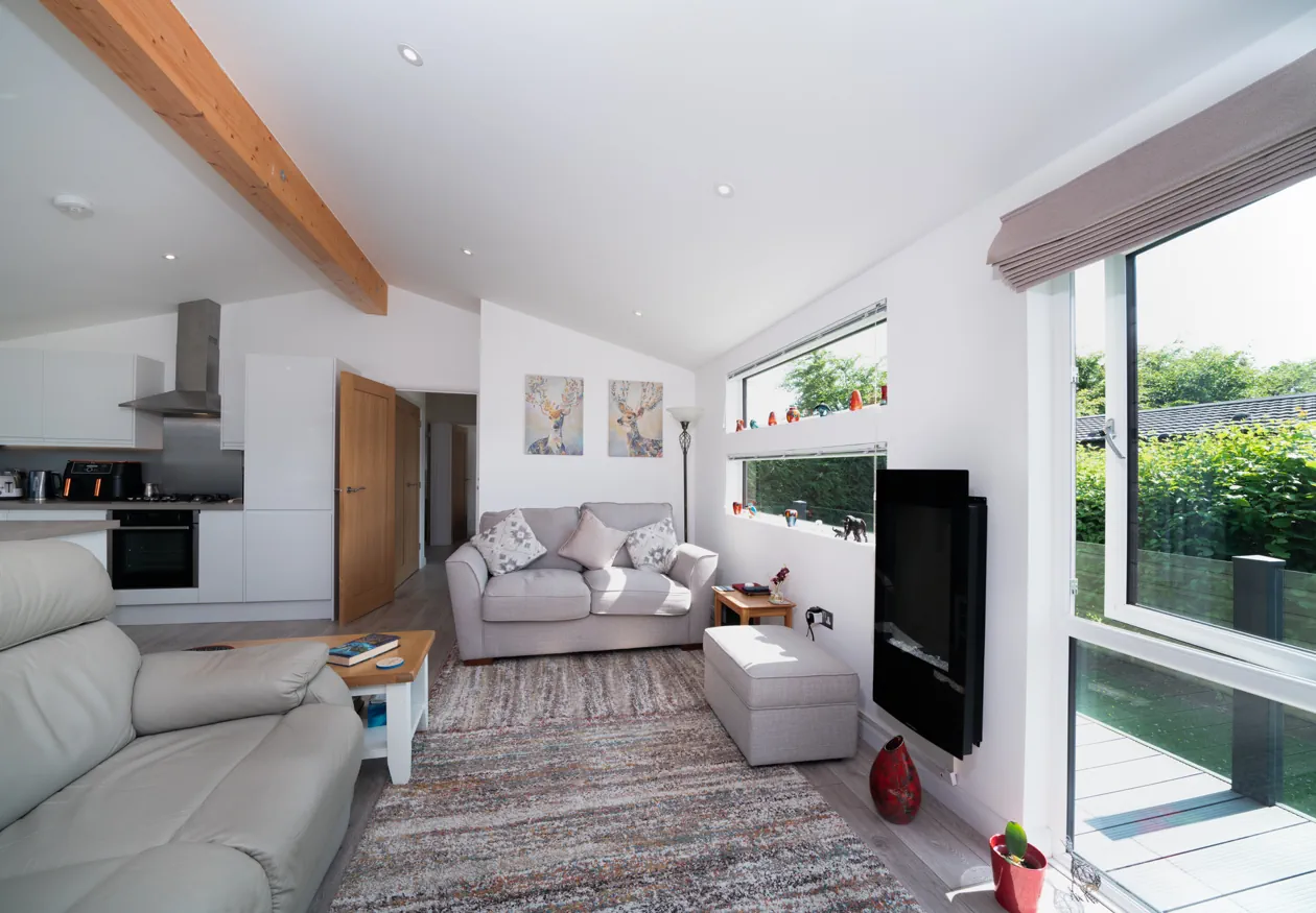 Light-filled holiday lodge interior featuring a spacious lounge, dining area, and modern kitchen with large windows overlooking landscaped grounds.