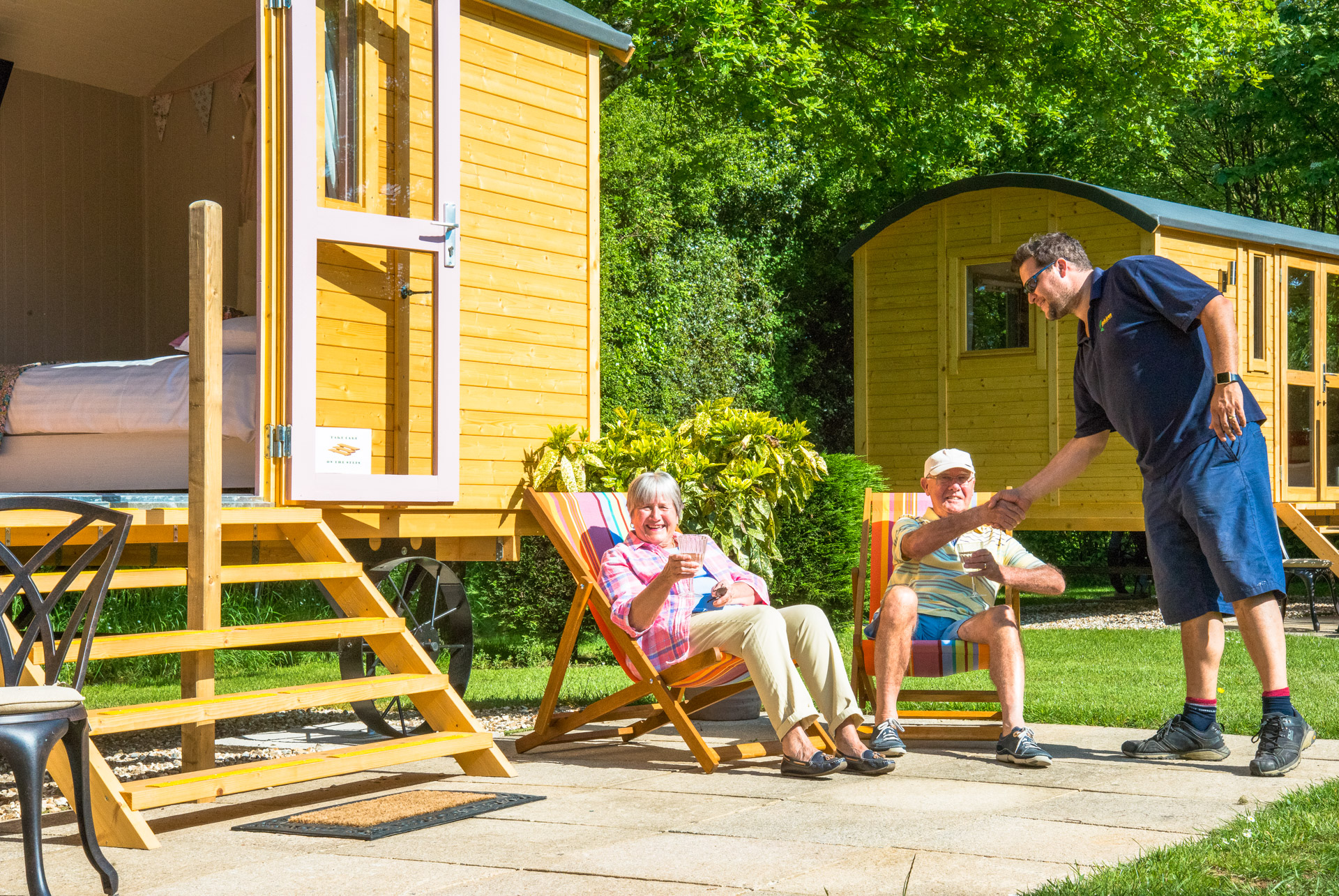 People relaxing in deckchairs outside a yellow shepherd hut, with a second hut alongside