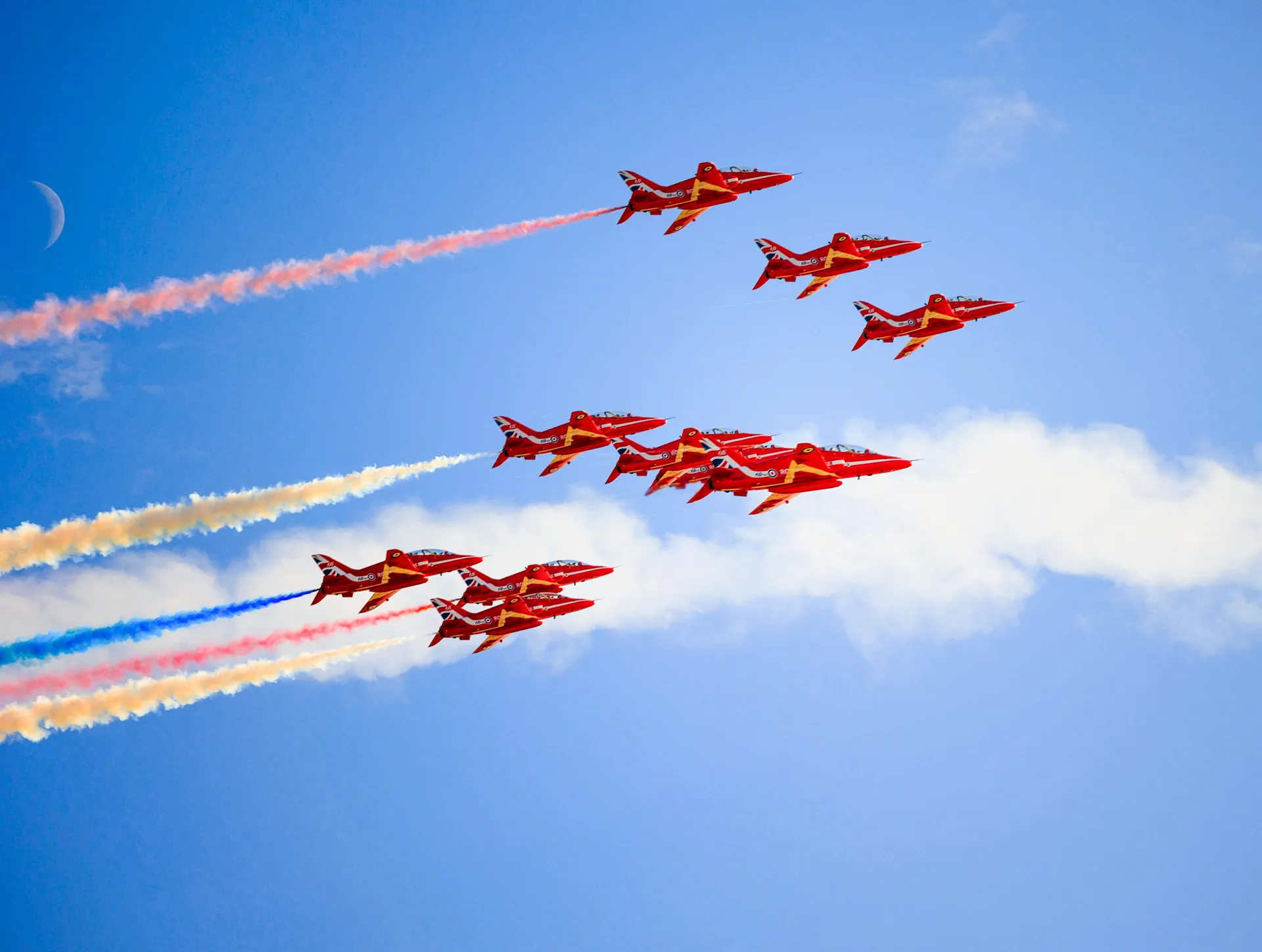 Red Arrows converging from two directions, smoke trails meeting against a blue sky